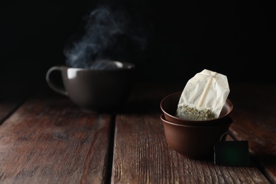 Photo of Bowls with used tea bag on wooden table. Space for text