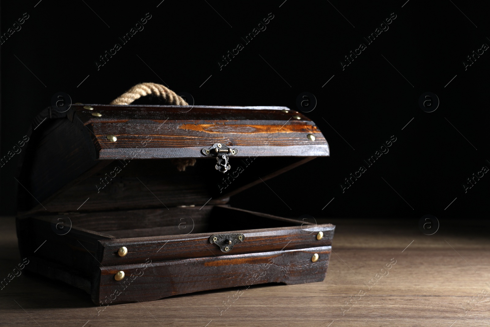 Photo of Empty treasure chest on wooden table against black background. Space for text