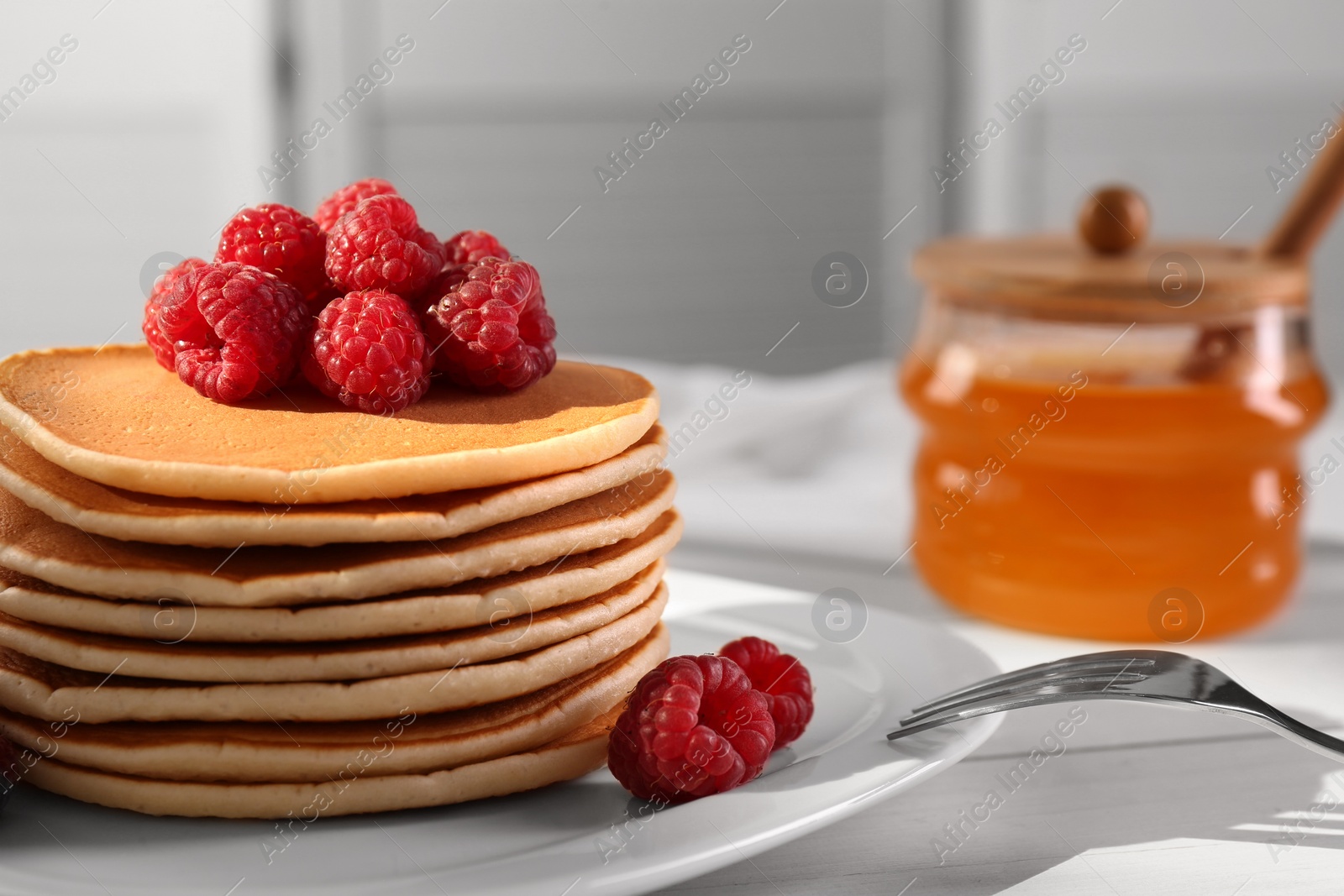 Photo of Stack of tasty pancakes with raspberries on white wooden table, closeup. Space for text