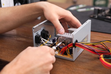 Male technician repairing power supply unit at table, closeup