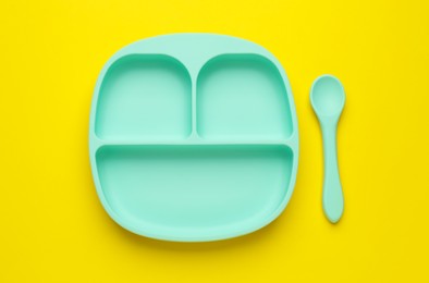 Photo of Plastic section plate and spoon on yellow background, flat lay. Serving baby food