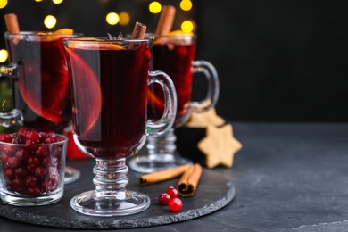 Photo of Aromatic mulled wine on black table against blurred festive lights, space for text