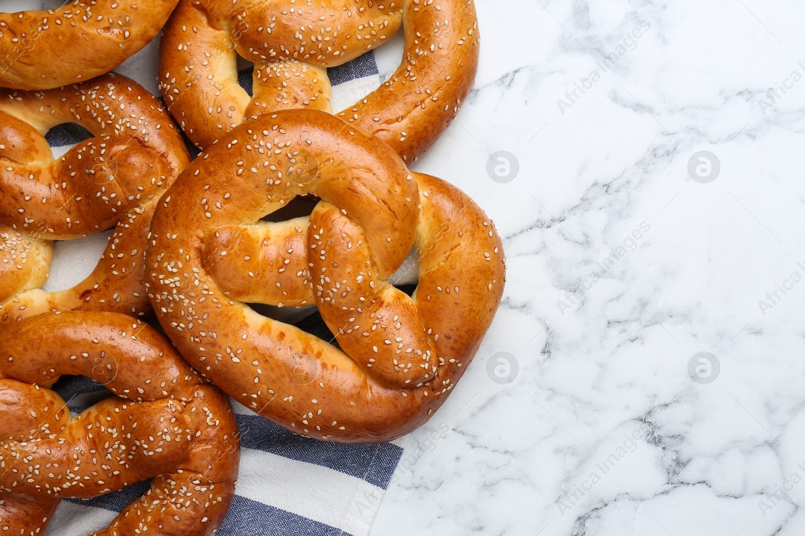 Photo of Delicious pretzels with sesame seeds on white marble table, flat lay. Space for text