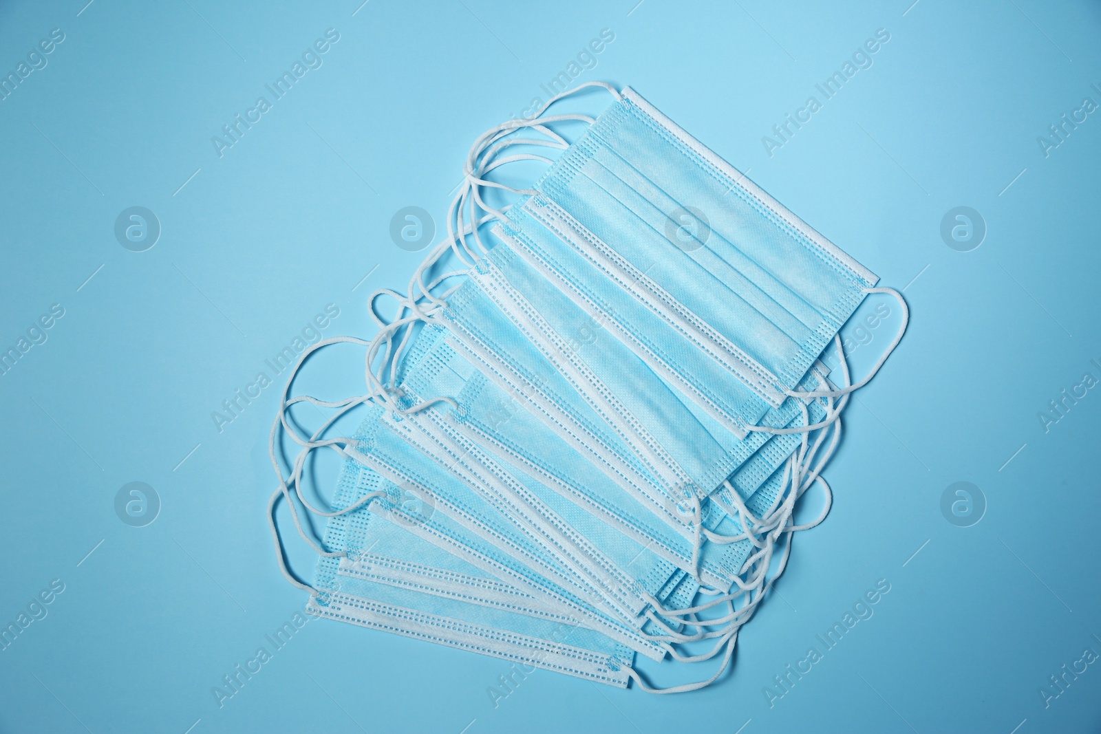 Photo of Disposable face masks on light blue background, flat lay. Protective measures during coronavirus quarantine