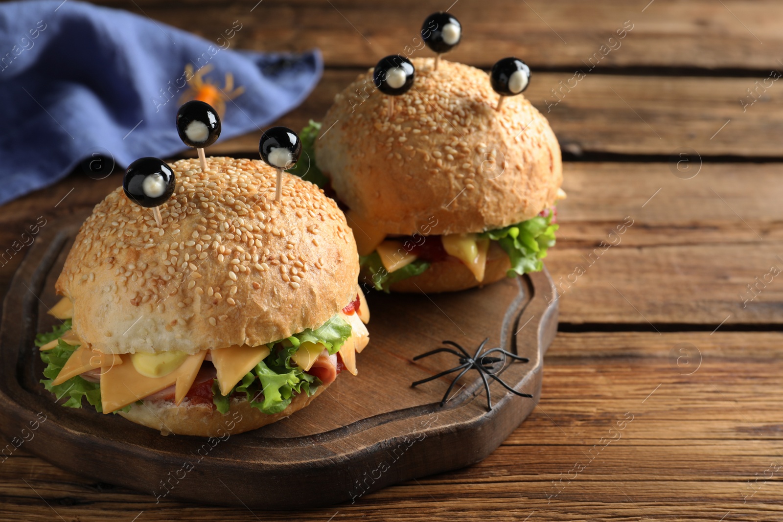 Photo of Cute monster burgers served on wooden table. Halloween party food