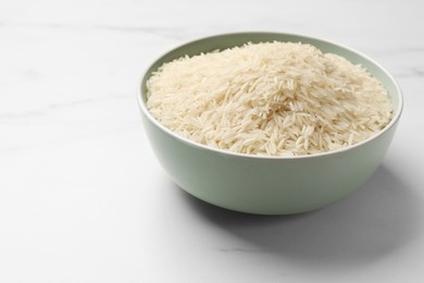 Photo of Raw basmati rice in bowl on white marble table, space for text