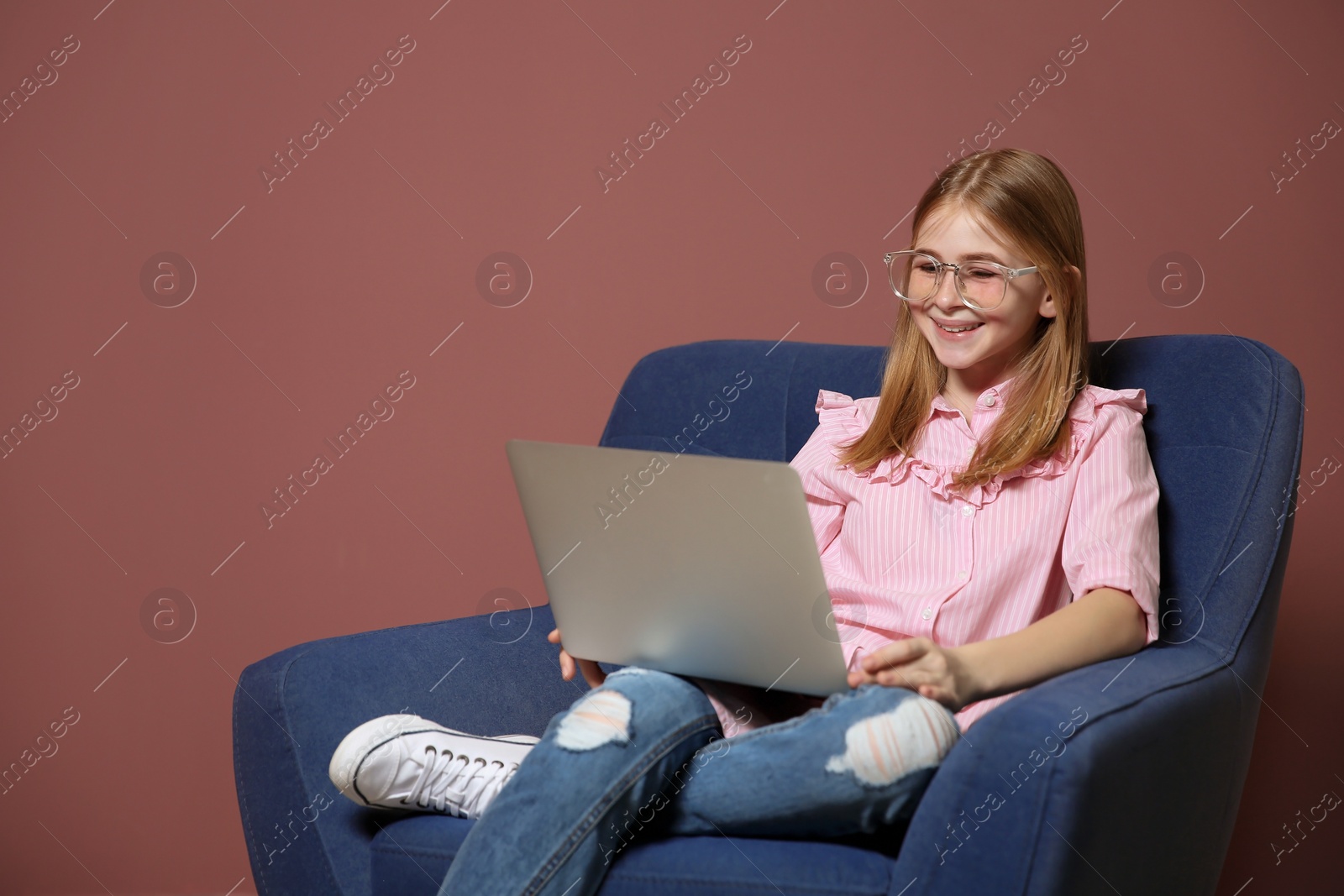 Photo of Cute teenage blogger with laptop sitting in armchair against color wall