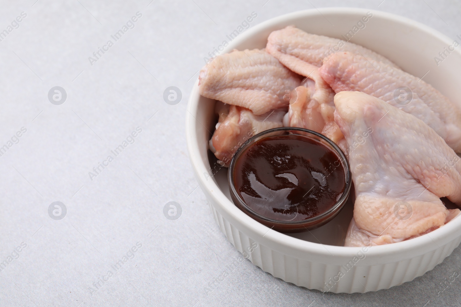 Photo of Plate with marinade and raw chicken wings on light textured table, closeup. Space for text