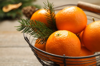 Photo of Fresh tangerines with fir tree branch in metal basket on wooden table, closeup. Christmas atmosphere