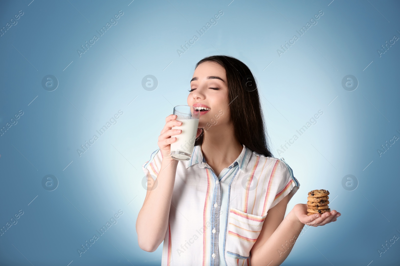 Photo of Beautiful young woman drinking milk with cookies on color background