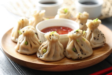 Photo of Wooden plate with tasty baozi dumplings and sauce on table, closeup