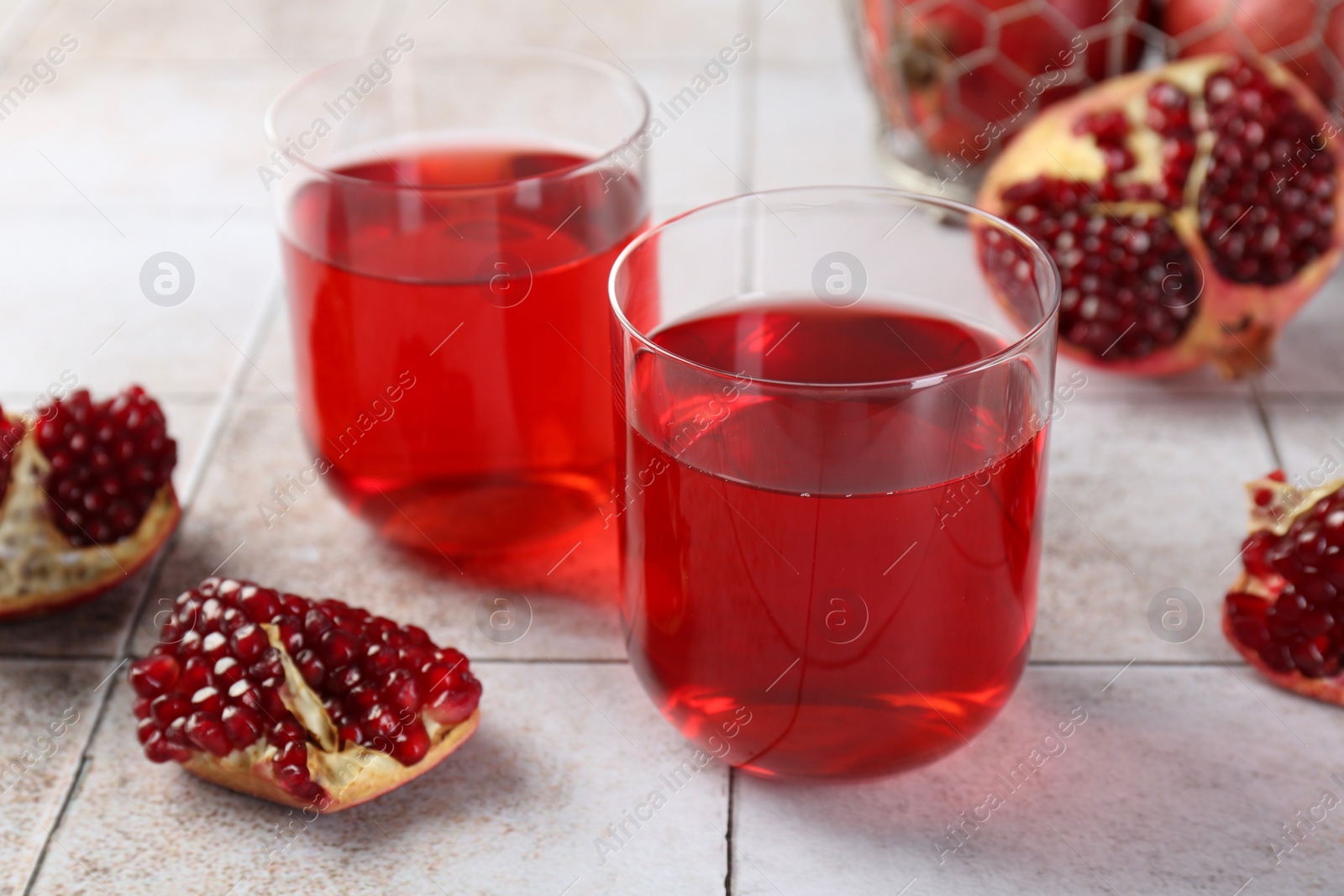 Photo of Tasty pomegranate juice in glasses and fresh fruits on white tiled table