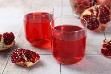 Photo of Tasty pomegranate juice in glasses and fresh fruits on white tiled table