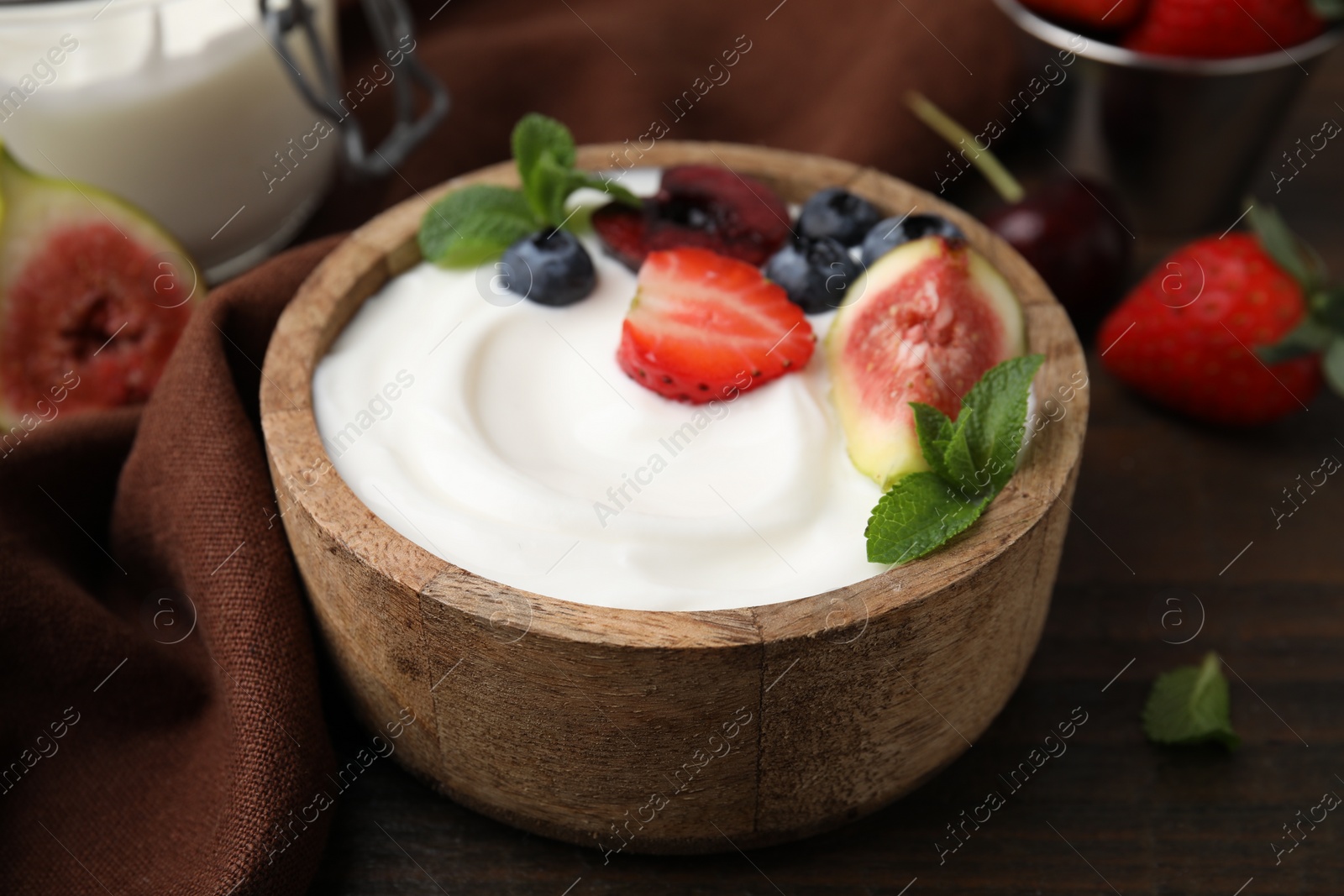 Photo of Bowl with yogurt, berries, fruits and mint on wooden table, closeup