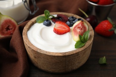 Bowl with yogurt, berries, fruits and mint on wooden table, closeup