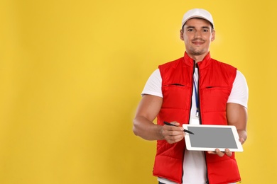 Photo of Happy young courier with tablet on yellow background. Space for text