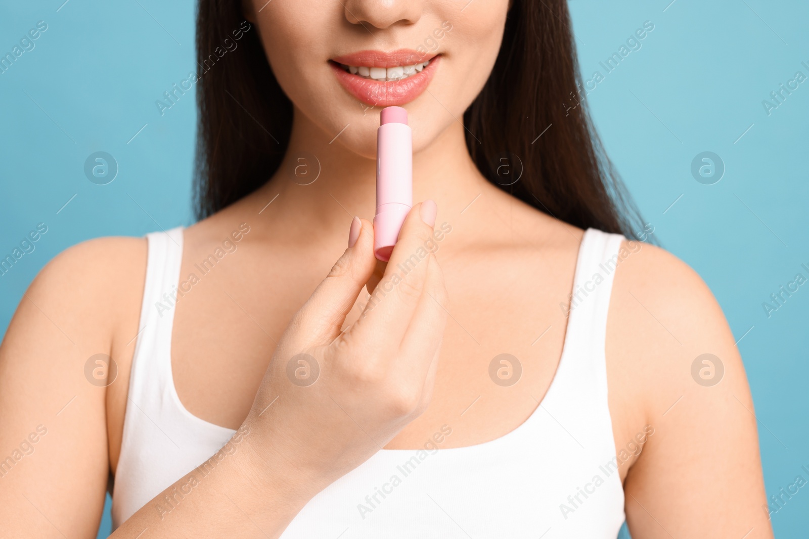 Photo of Young woman applying lip balm on turquoise background, closeup