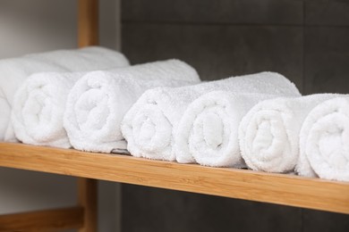 Rolled soft terry towels on wooden shelf indoors, closeup