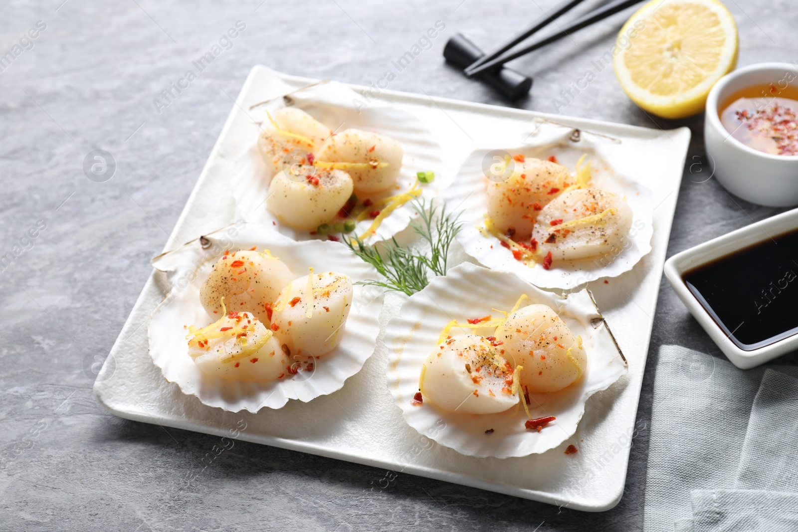 Photo of Raw scallops with spices, dill, lemon zest and shells on grey marble table, closeup