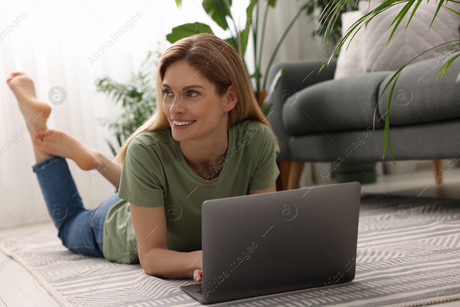 Photo of Woman using laptop on floor in room with beautiful potted houseplants