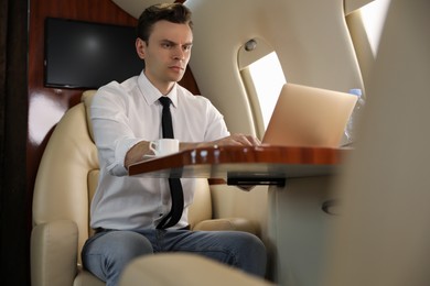 Photo of Businessman working on laptop at table in airplane during flight