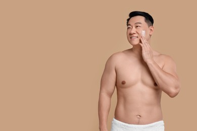 Handsome man applying cream onto his face on light brown background. Space for text