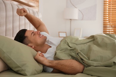 Man stretching in bed with green linens at home
