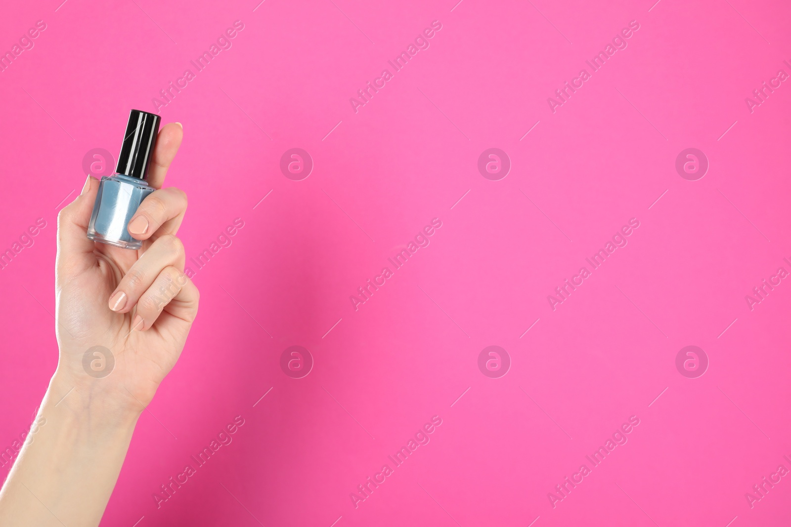 Photo of Woman holding nail polish on pink background, closeup. Space for text