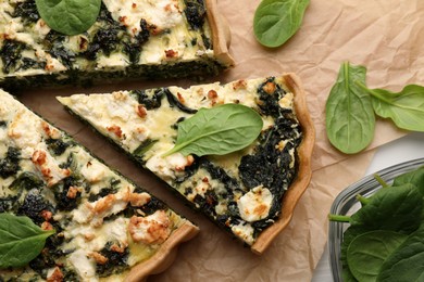 Delicious homemade quiche and fresh spinach leaves on parchment paper, flat lay