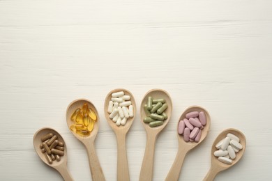 Photo of Different vitamin capsules in spoons on white wooden table, flat lay. Space for text