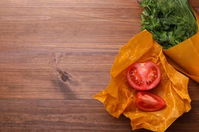 Photo of Slices of fresh tomato and herbs in beeswax food wraps on wooden table, top view. Space for text