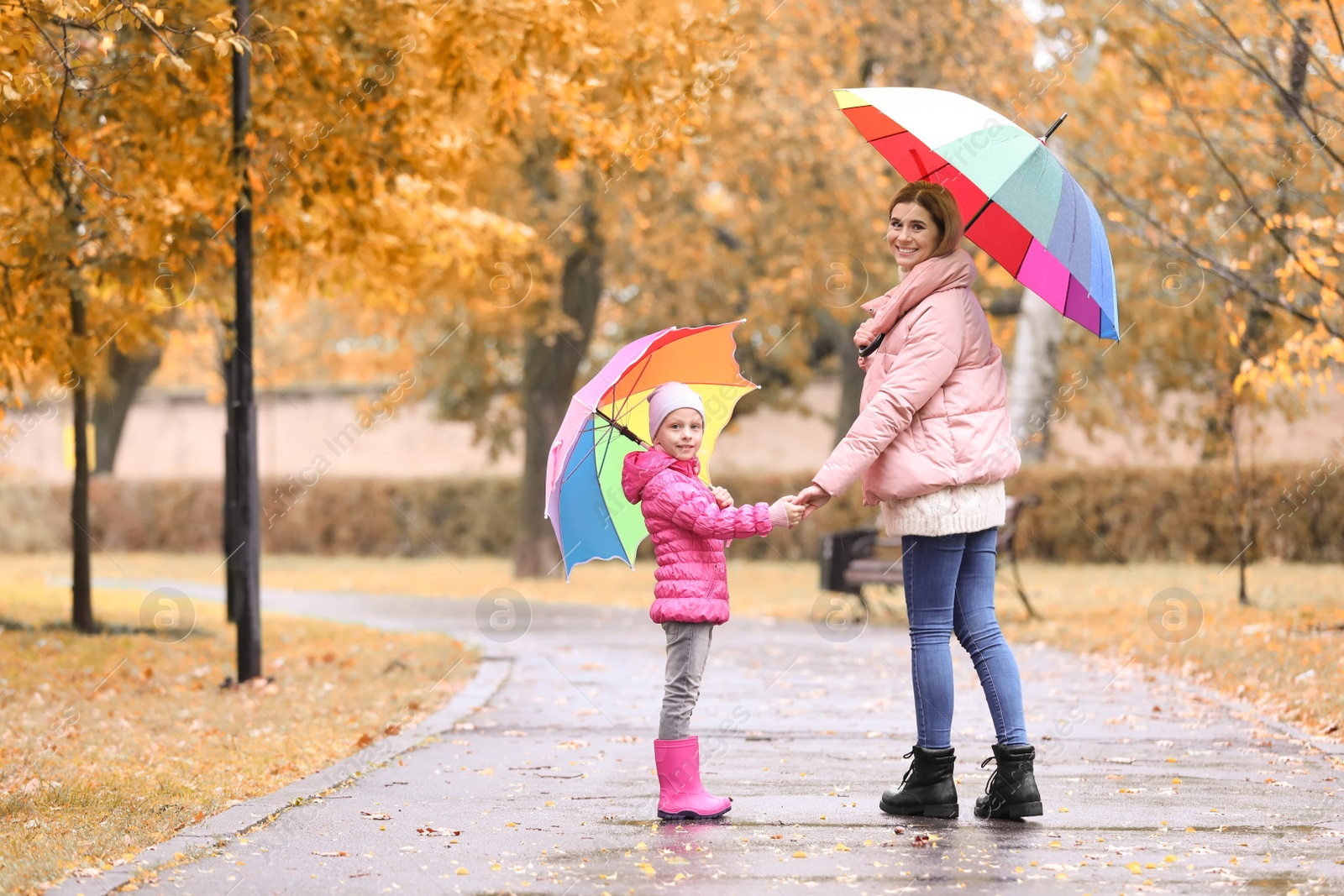 Photo of Mother and daughter with umbrellas taking walk in autumn park on rainy day