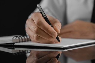 Photo of Man writing in notebook at black table, closeup