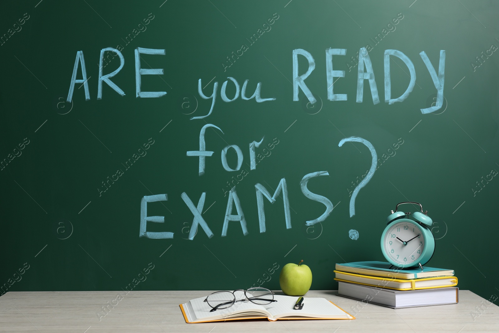 Photo of Different stationery and alarm clock on wooden table near chalkboard with phrase Are You Ready For Exams