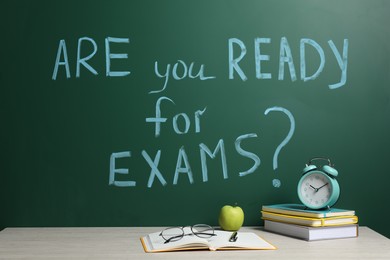 Different stationery and alarm clock on wooden table near chalkboard with phrase Are You Ready For Exams