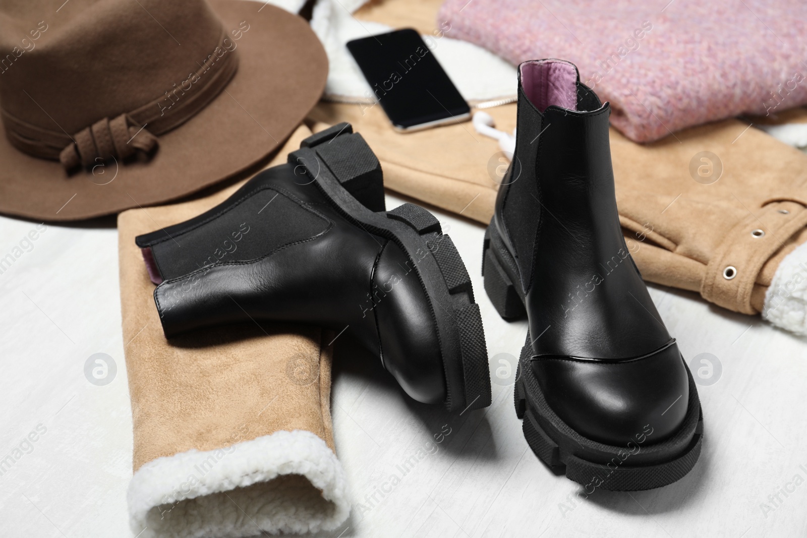 Photo of Black leather boots, clothes and accessories on white wooden background