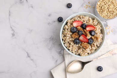 Photo of Tasty oatmeal with strawberries, blueberries and walnuts served on white marble table, flat lay. Space for text