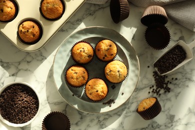 Photo of Delicious sweet muffins with chocolate chips on white marble table, flat lay