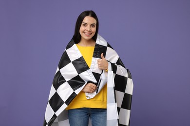 Photo of Happy young woman with checkered flag showing thumbs up on violet background
