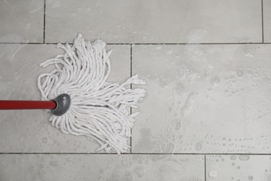Photo of Cleaning grey tiled floor with string mop, top view. Space for text