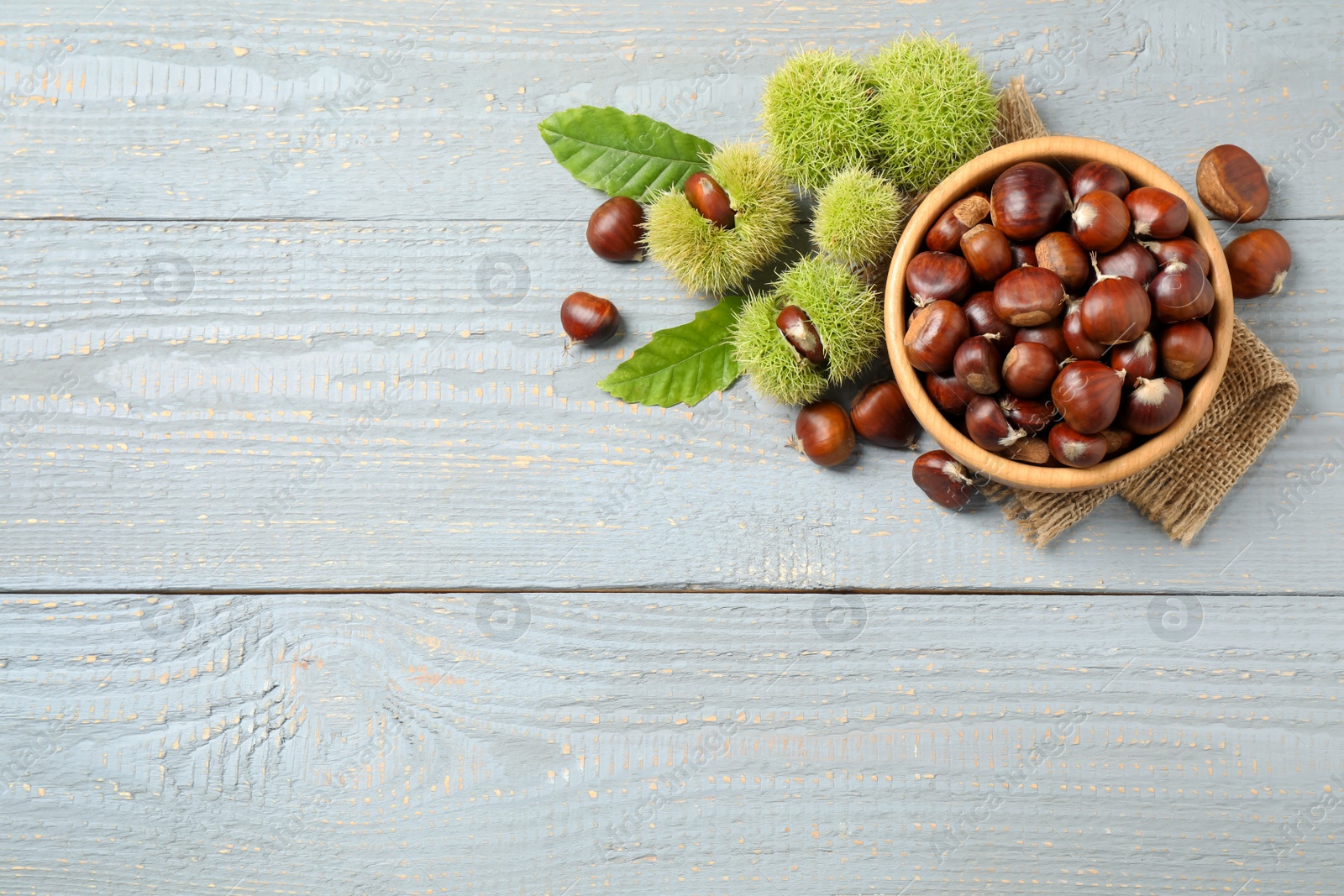Photo of Fresh sweet edible chestnuts on grey wooden table, flat lay. Space for text