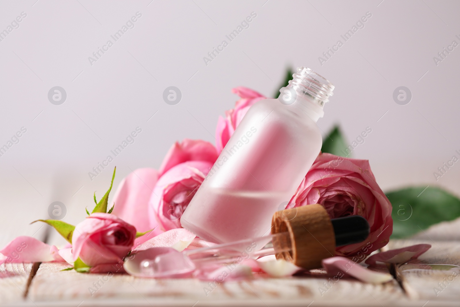 Photo of Bottle of essential oil and roses on white wooden table against light background
