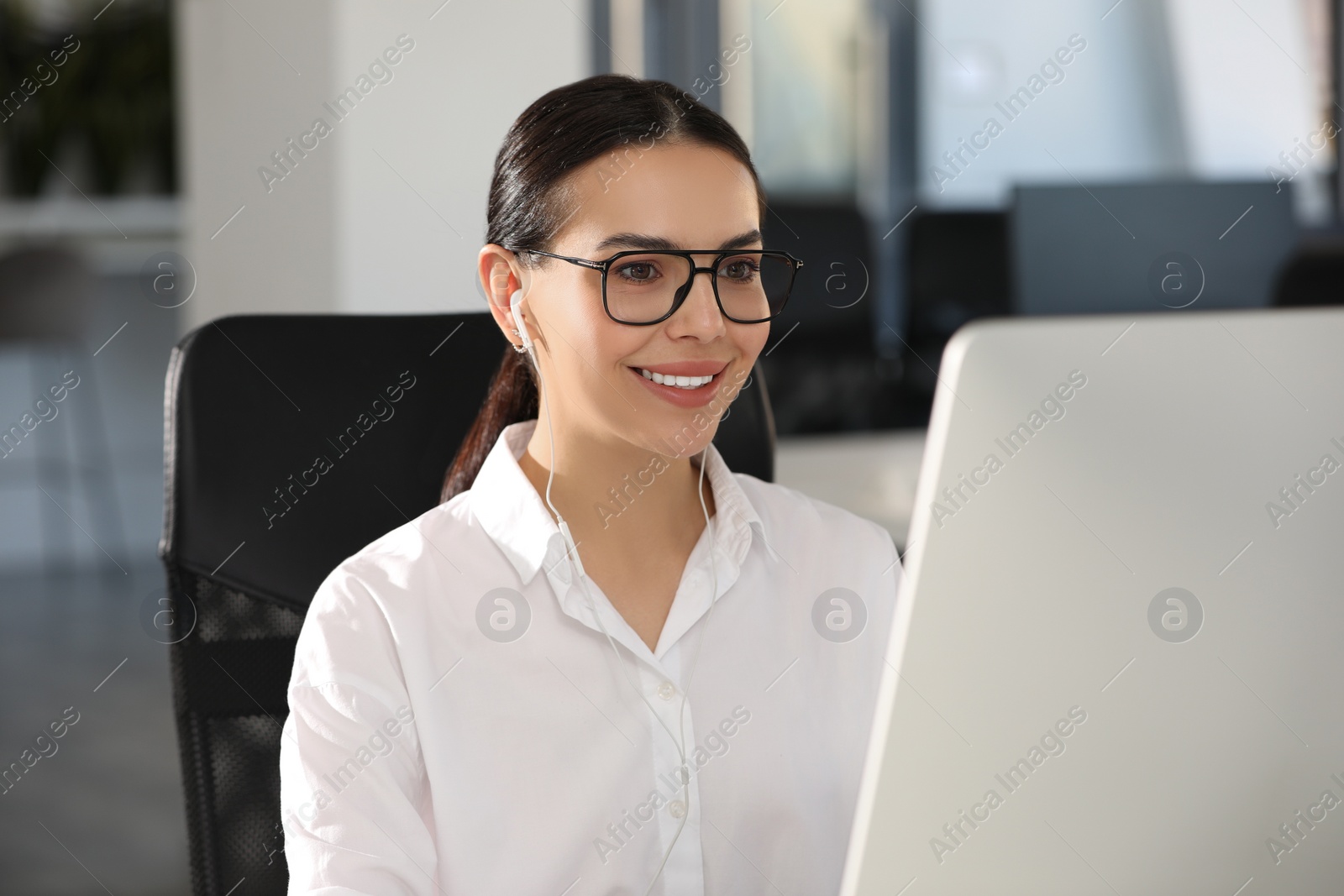 Photo of Happy woman with earphones using modern computer in office