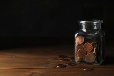 Photo of Glass jar with coins on wooden table, space for text