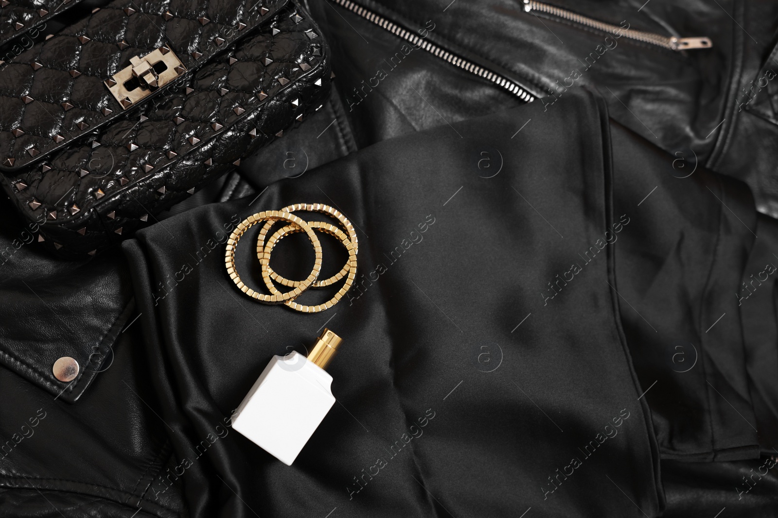 Photo of Leather bag, bottle of perfume and golden bracelets on black fabric, flat lay. Space for text