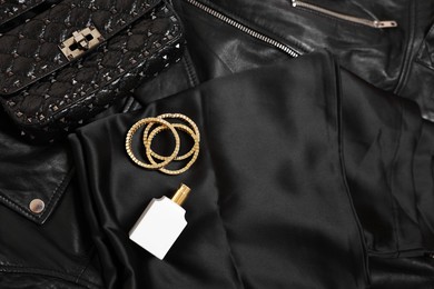Photo of Leather bag, bottle of perfume and golden bracelets on black fabric, flat lay. Space for text