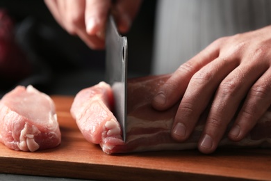 Photo of Man cutting fresh raw meat on wooden board, closeup