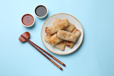 Photo of Fried spring rolls and sauces served on light blue table, top view