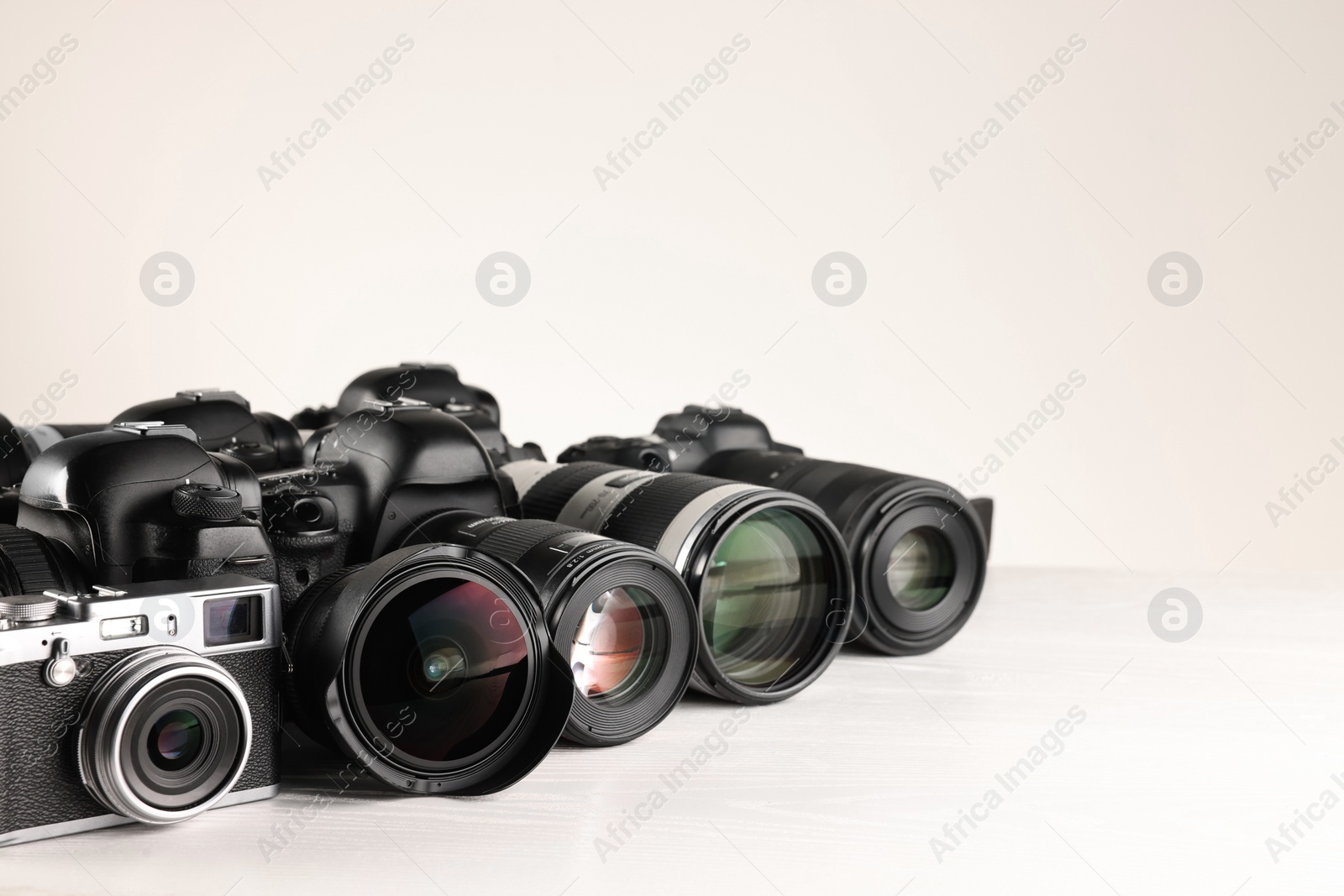 Photo of Modern cameras on white wooden table, space for text