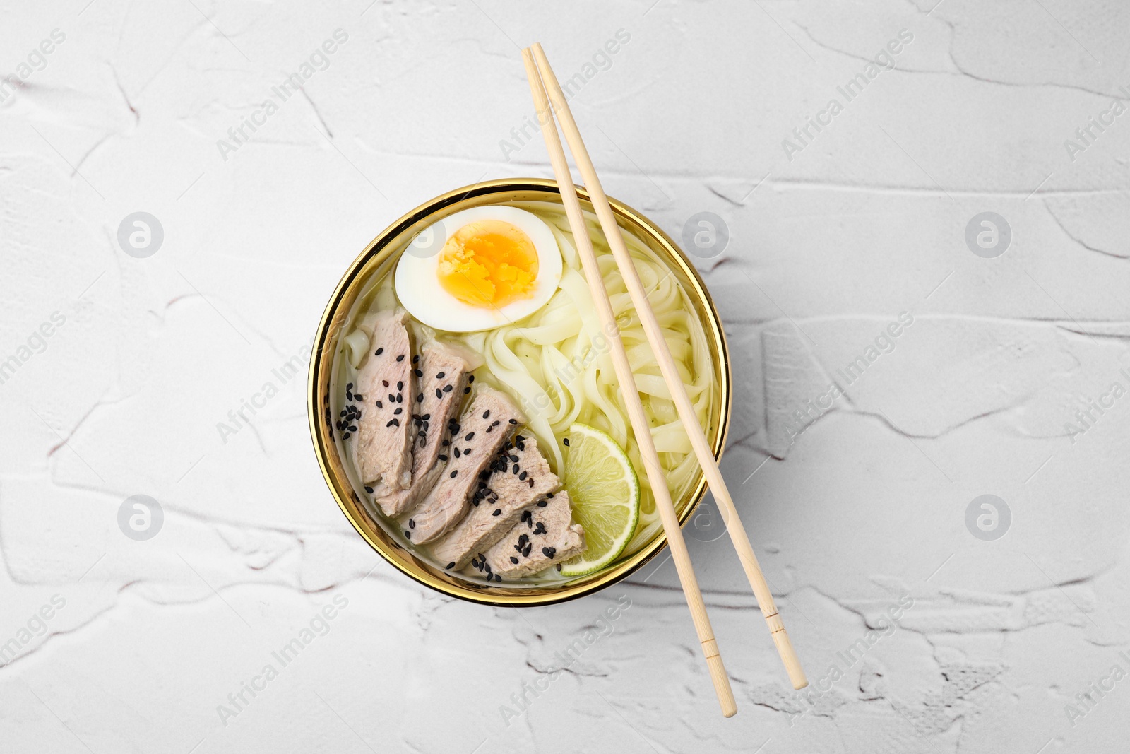 Photo of Bowl of delicious rice noodle soup with meat and egg on white textured table, top view